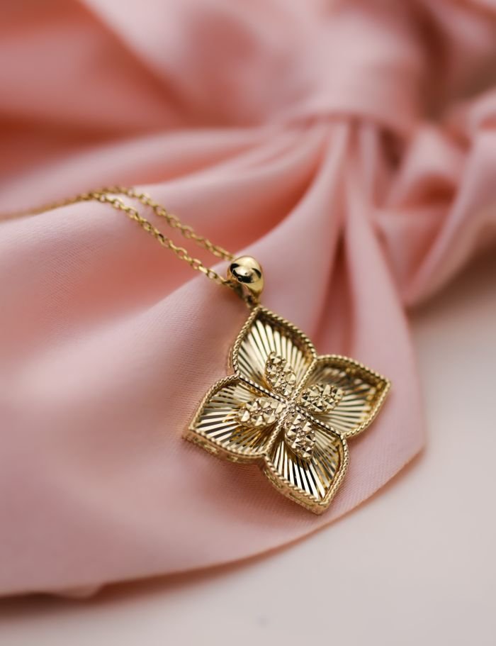 Close-up of a gold flower pendant necklace on elegant pink fabric, showcasing luxury and style.