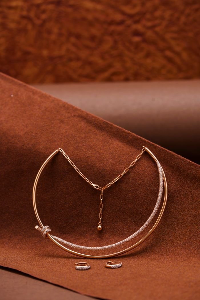 Stylish rose gold necklace and rings on textured brown fabric backdrop perfect for fashion advertising.