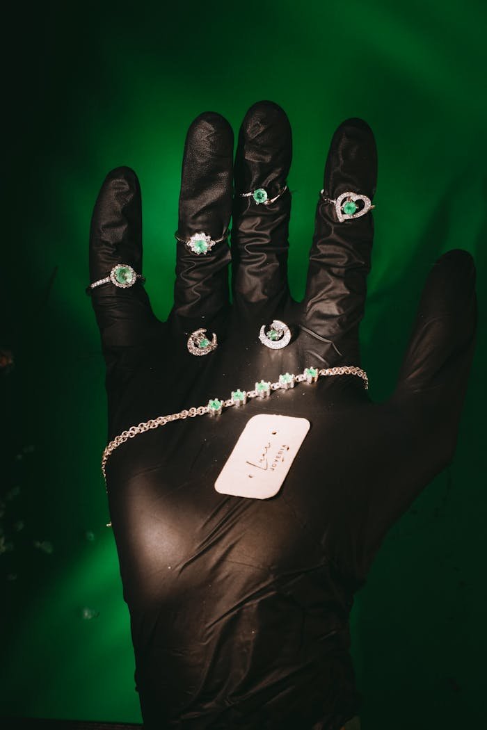 Luxurious emerald jewelry collection showcased on black glove, set against a vibrant green background.