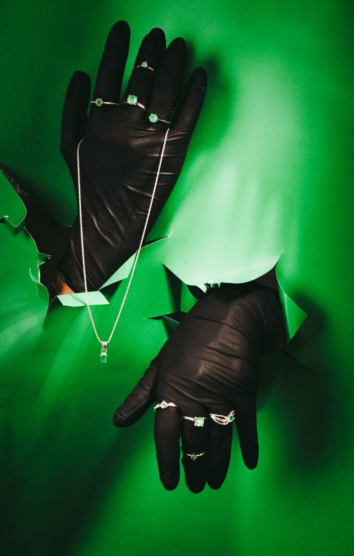 Artistic jewelry presentation with black gloved hands against green background.