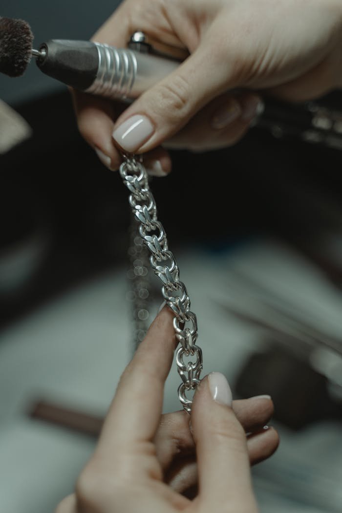 Close-up of a jeweler polishing a silver chain with a tool, showcasing craftsmanship and precision.