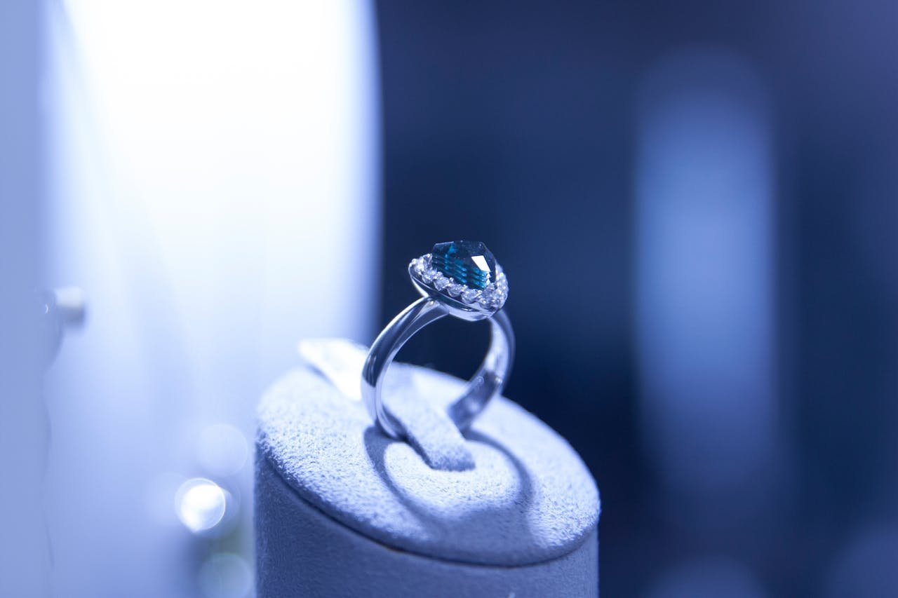about-img Close-up of an elegant silver ring with a blue gemstone, showcasing luxury and elegance.